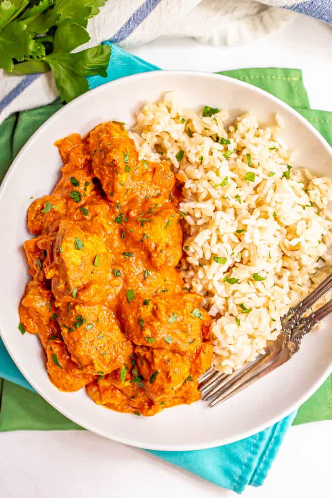 A plated serving of chicken tikka masala alongside steamed brown rice and chopped parsley