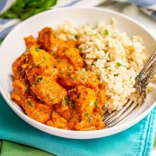 A plated serving of chicken tikka masala alongside steamed brown rice with two forks alongside
