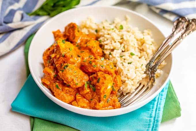 A plated serving of chicken tikka masala alongside steamed brown rice with two forks alongside