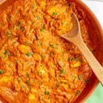 A large skillet with a wooden spoon picking up some chicken tikka masala