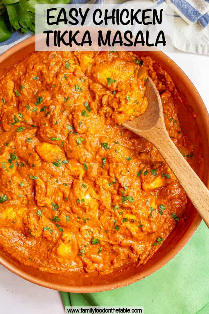 A large skillet with a wooden spoon picking up some chicken tikka masala