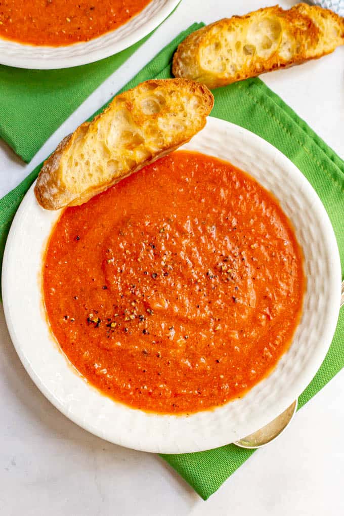 A bowl of homemade tomato soup with cracked black pepper and some toasted bread alongside