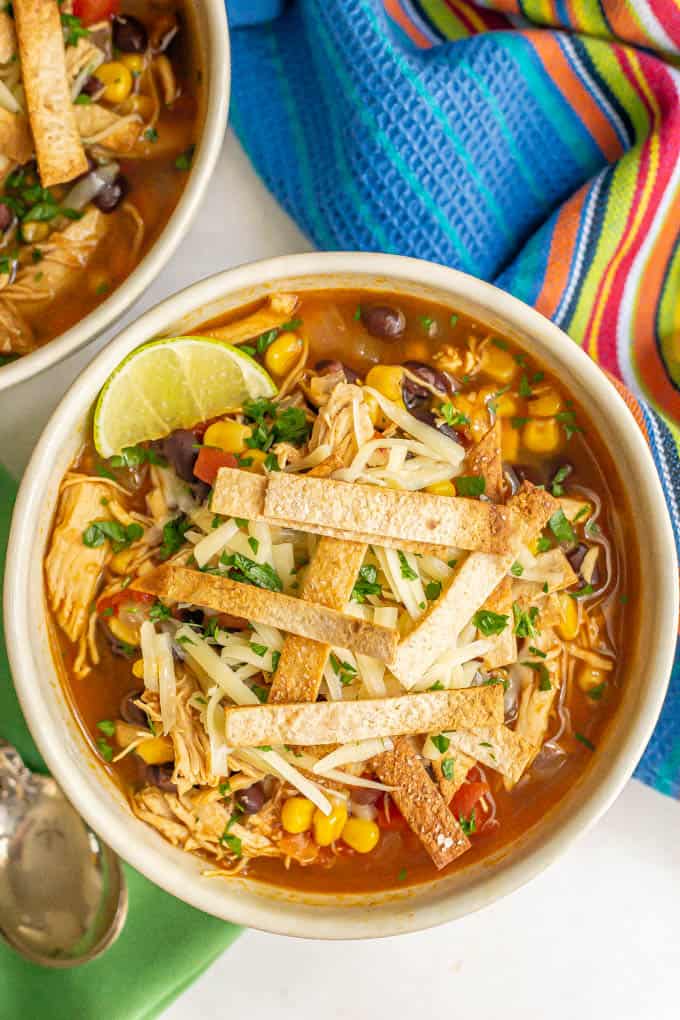 A bowl of chicken tortilla soup with black beans and corn, topped with tortilla strips, cheese and a lime wedge