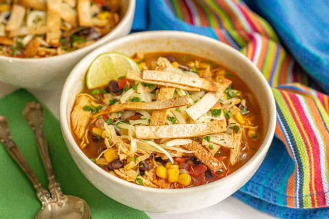 Crispy tortilla strips on top of a bowl of chicken soup with black beans and corn