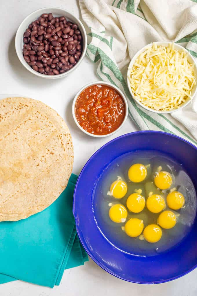 Breakfast burrito ingredients in separate bowls on a white marble counter