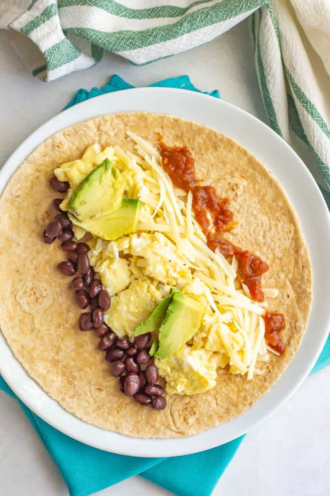 Black beans, eggs, cheese and salsa lined up on a tortilla with avocado slices on top