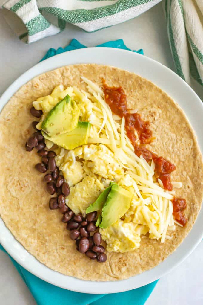 Tortilla with scrambled eggs, beans, cheese, salsa and avocado on a white plate