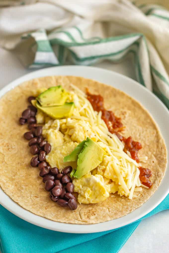 Breakfast burrito fillings laid onto a tortilla on a white plate