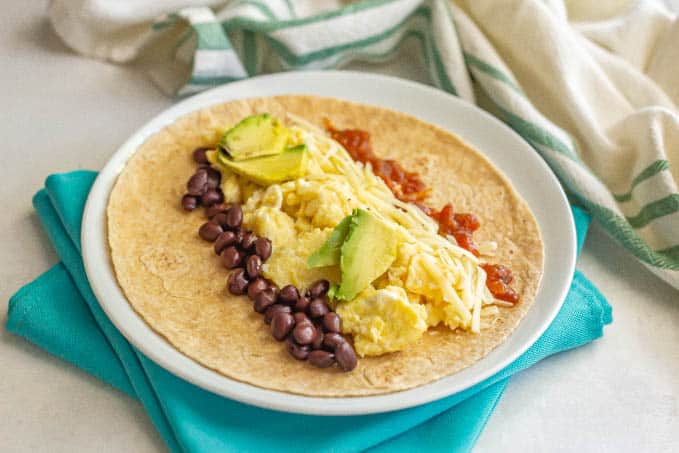 Breakfast burrito fillings laid onto a tortilla on a white plate set on turquoise napkins