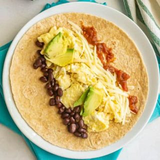 Vegetarian breakfast burrito fillings laid onto a tortilla on a white plate
