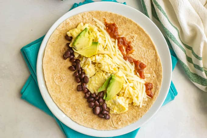 Vegetarian breakfast burrito fillings laid onto a tortilla on a white plate