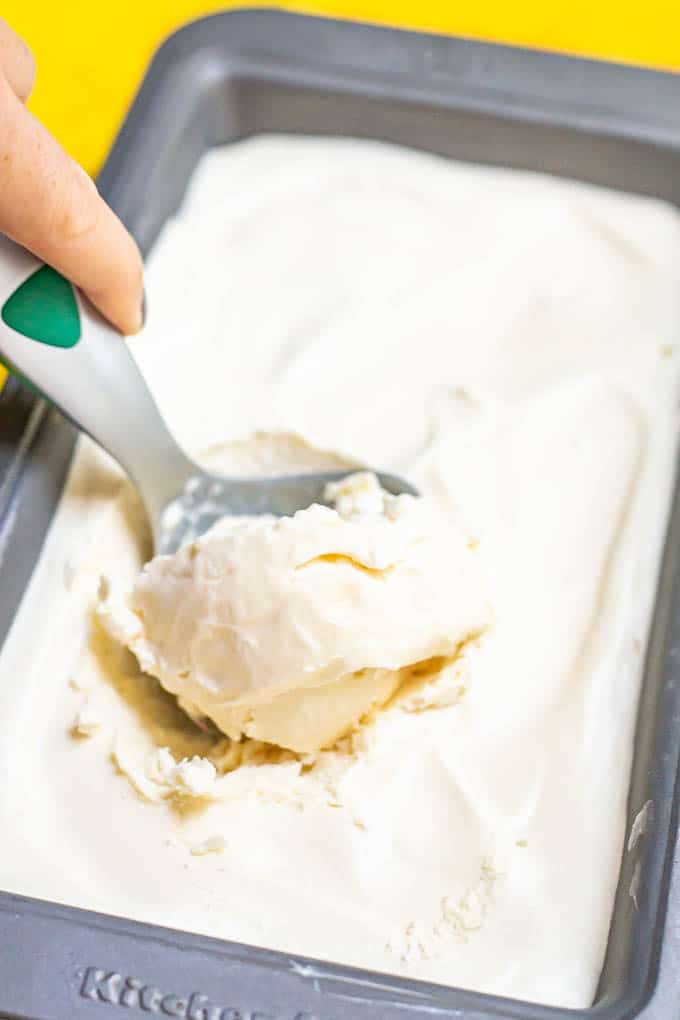 An ice cream scoop taking a scoop of vanilla ice cream from a bread pan