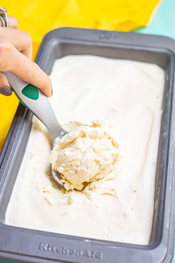 A hand scooping vanilla ice cream from a bread pan after it's frozen