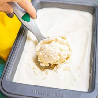 A hand scooping up a scoop of homemade vanilla ice cream from a bread pan