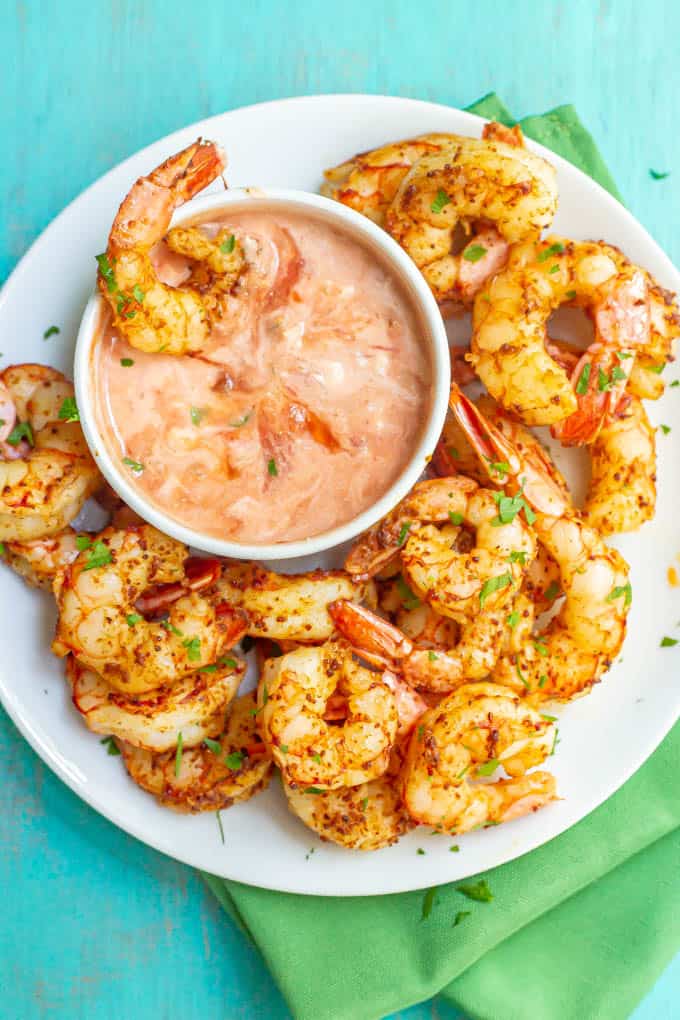 A shrimp resting in a bowl of dipping sauce on a plate with other shrimp