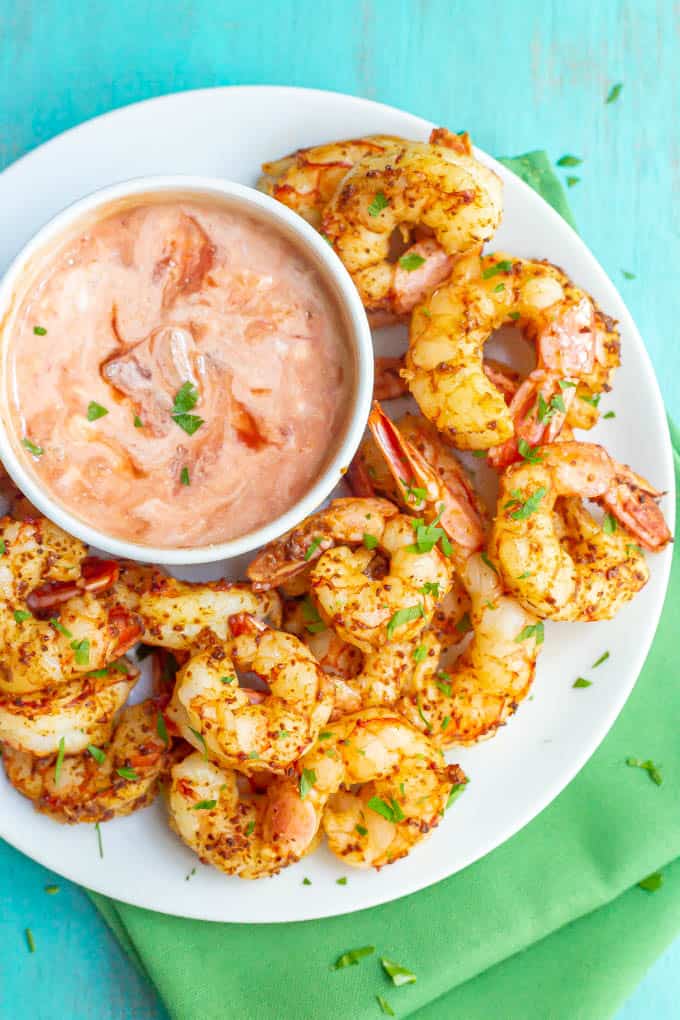 Cooked seasoned shrimp sprinkled with cilantro and served on a white plate with a dipping sauce