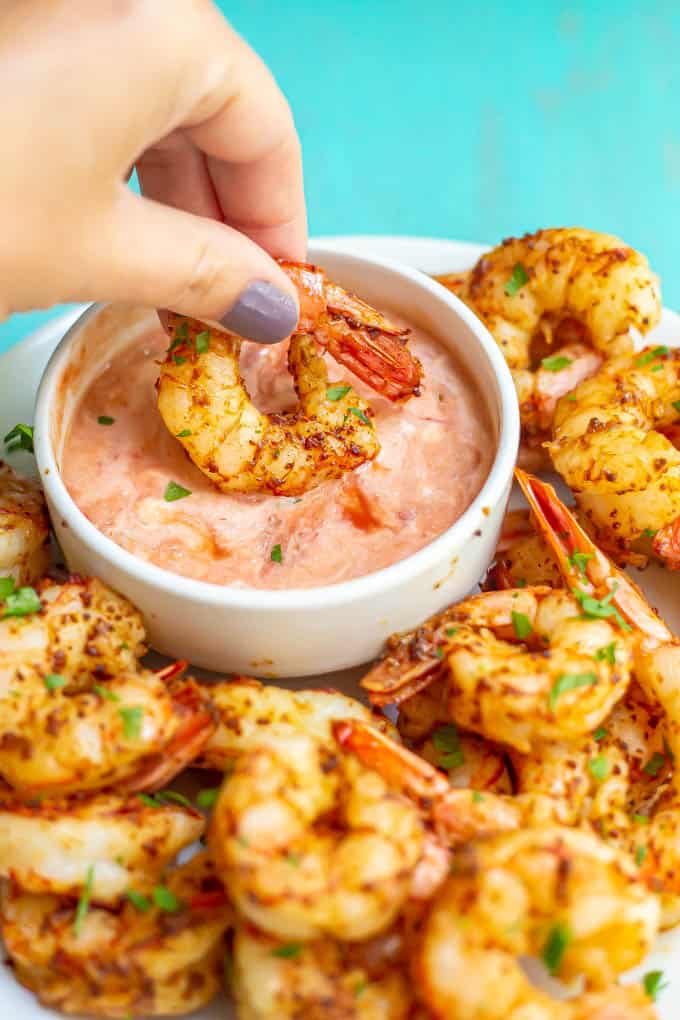 A hand dipping a shrimp in a creamy salsa