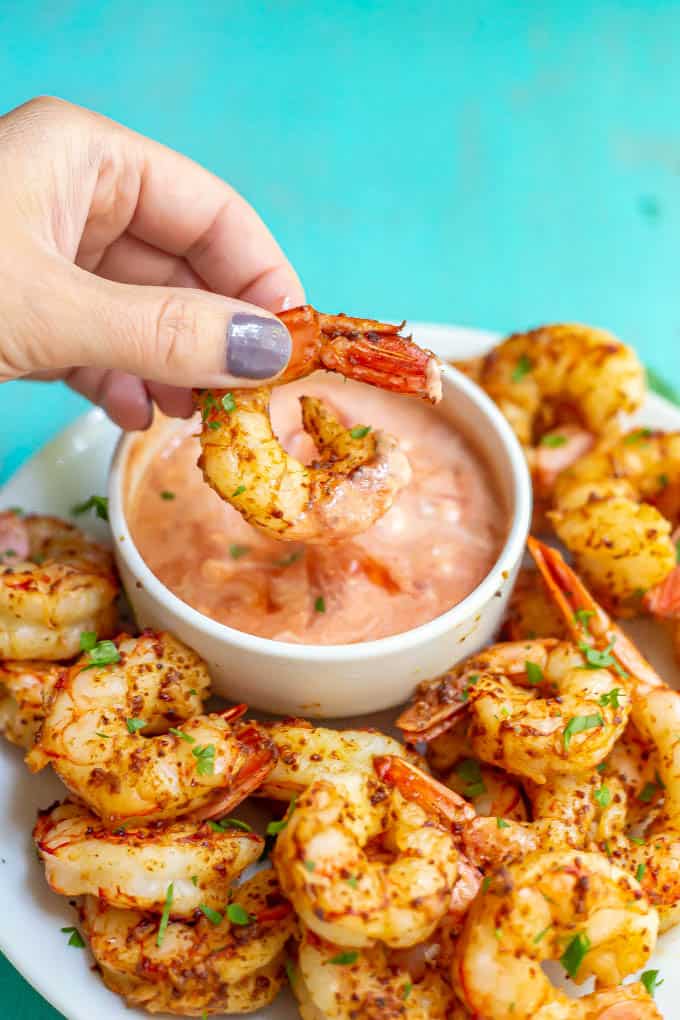 A hand holding a seasoned cooked shrimp that's been dipped in a sauce