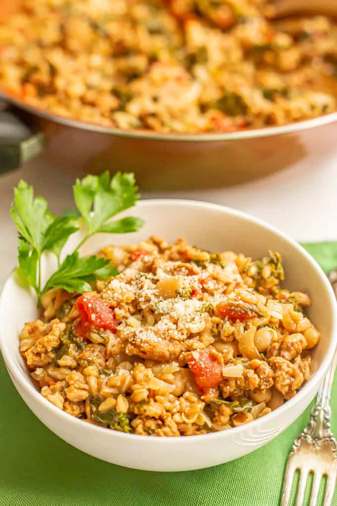 White bowl filled with a turkey sausage and farro mixture with veggies served on green napkins with a fork