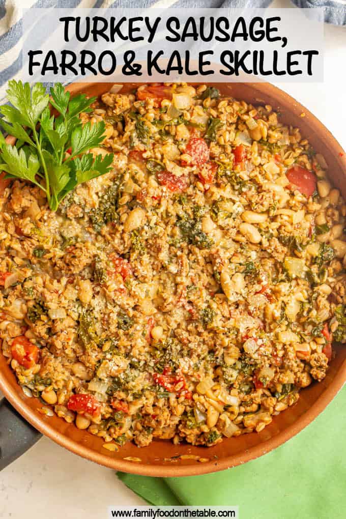 Large skillet with turkey sausage, farro, white beans, kale and tomatoes with a sprig of parsley