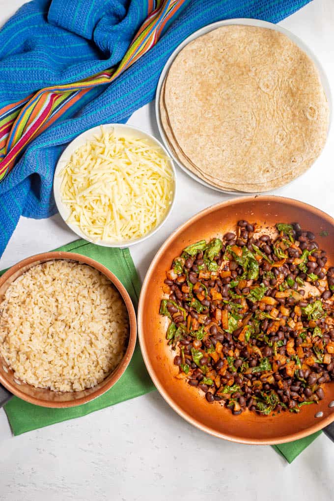 Ingredients laid out in separate pans and dishes for making vegetarian bean burritos