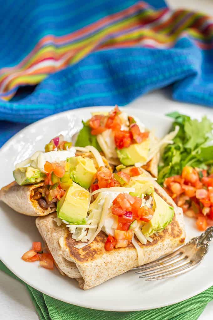 Vegetarian burritos loaded with tons of toppings and served on a white plate with a fork alongside