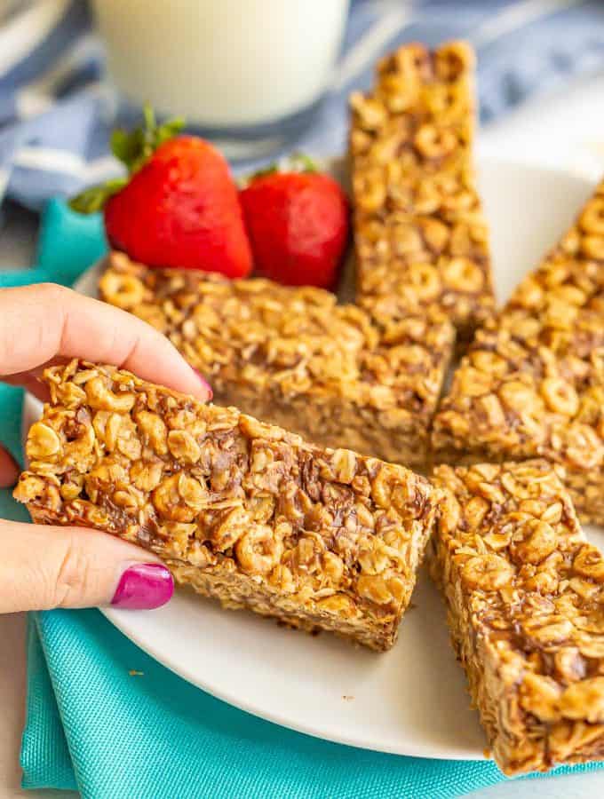 A hand picking up a breakfast bar from a white plate