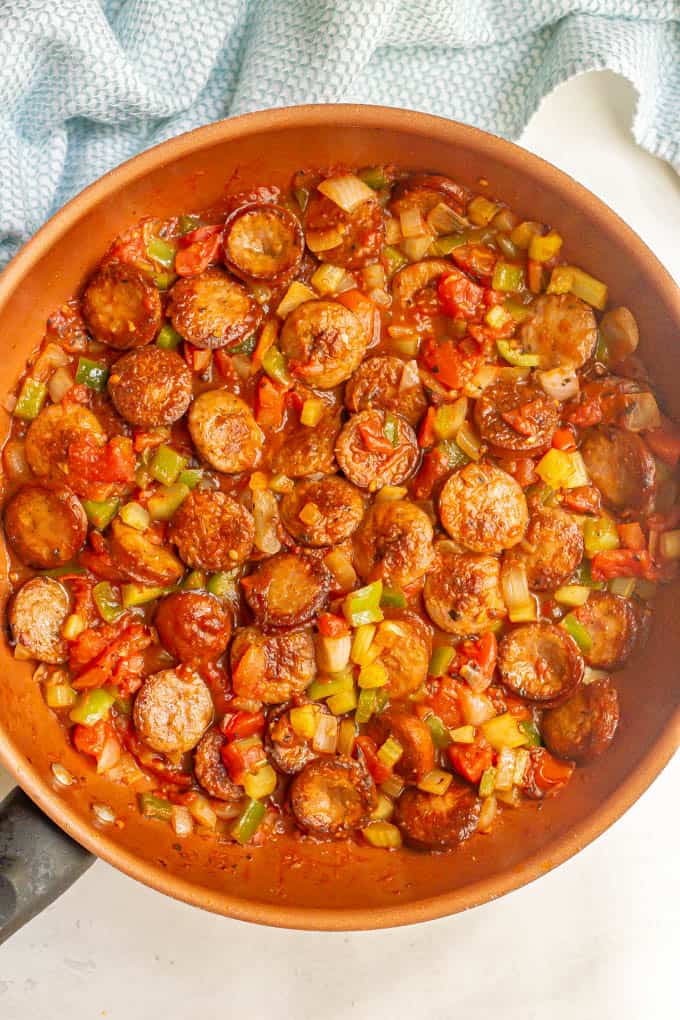 A skillet full fo cooked sausages, tomatoes and veggies
