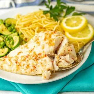 A piece of cooked cod with sauce served with noodles and veggies on a white plate