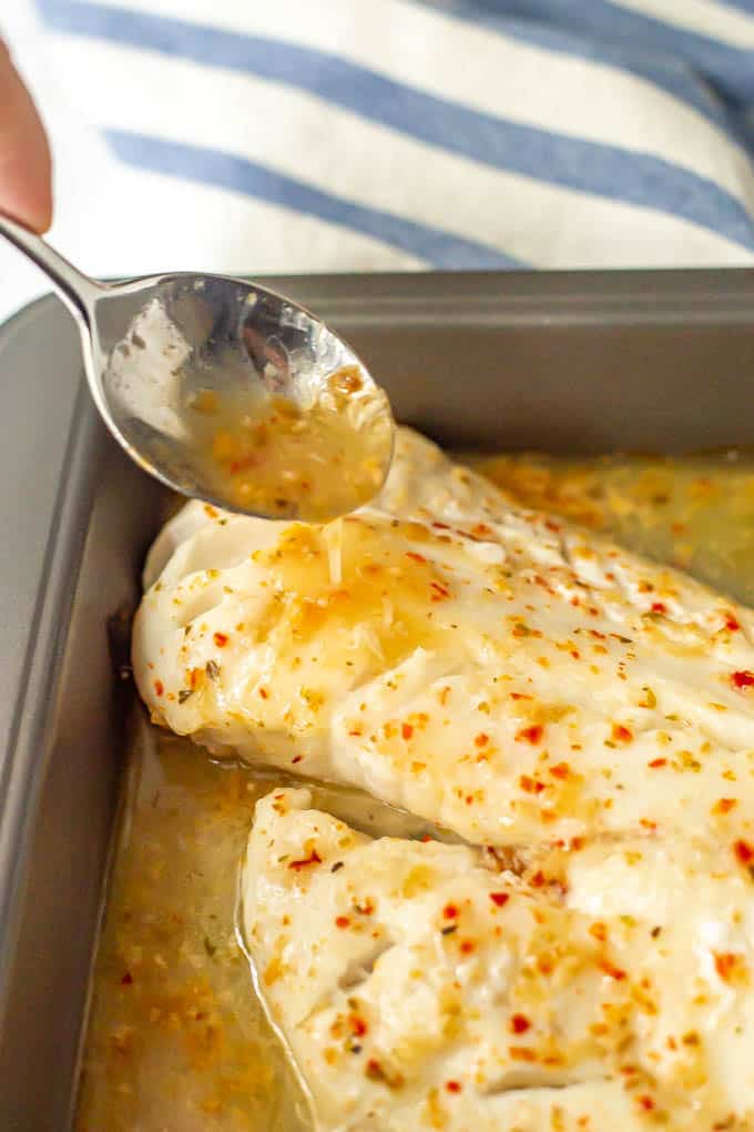 A spoon drizzling Italian dressing over baked white fish in a pan