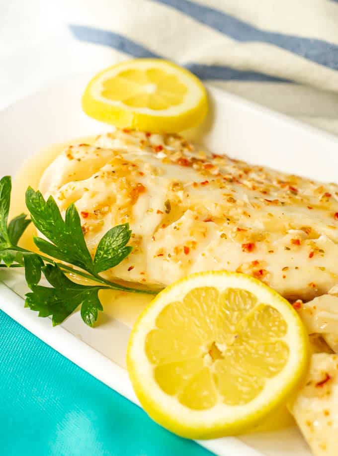 Baked cod with Italian dressing served on a white platter with lemon slices and parsley as garnishes