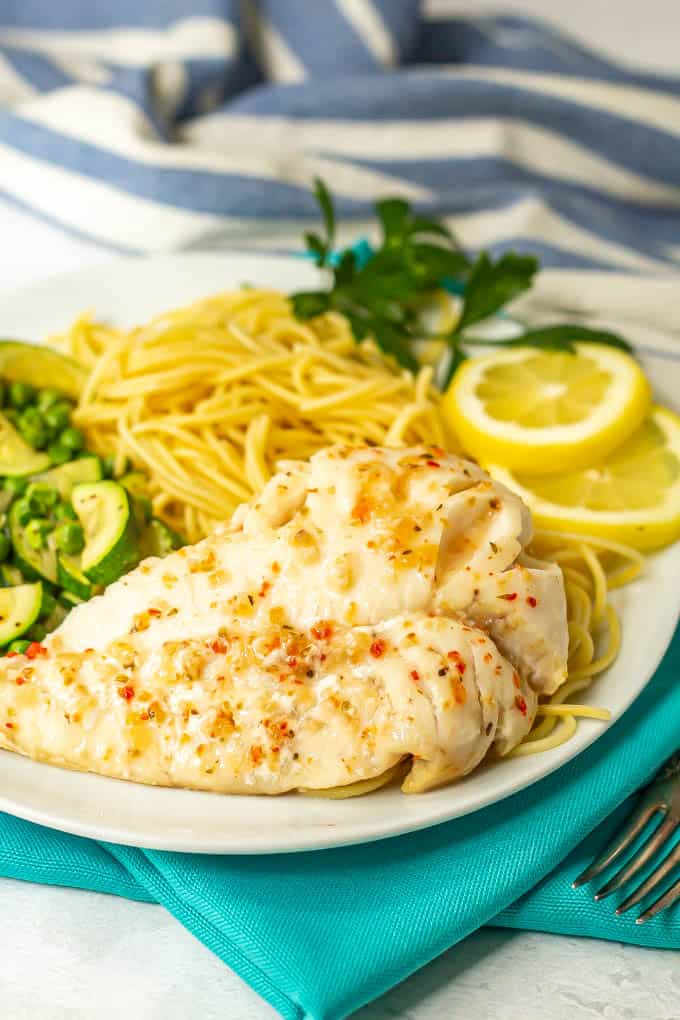 A filet of cooked cod with sauce served with noodles and veggies on a white plate