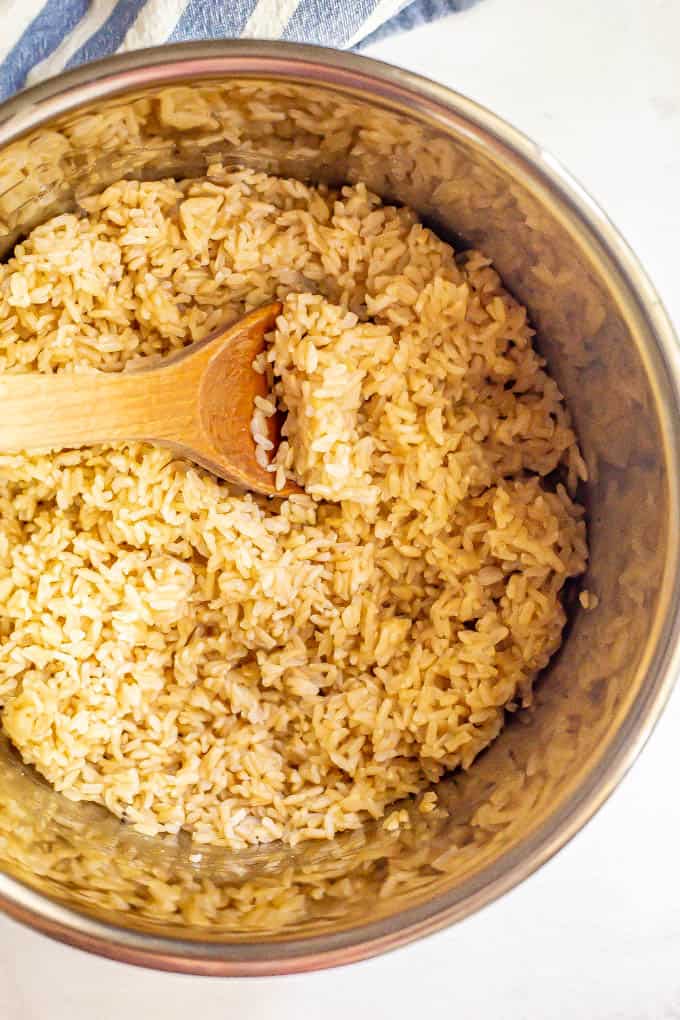 A wooden spoon resting in a pressure cooker with cooked brown rice