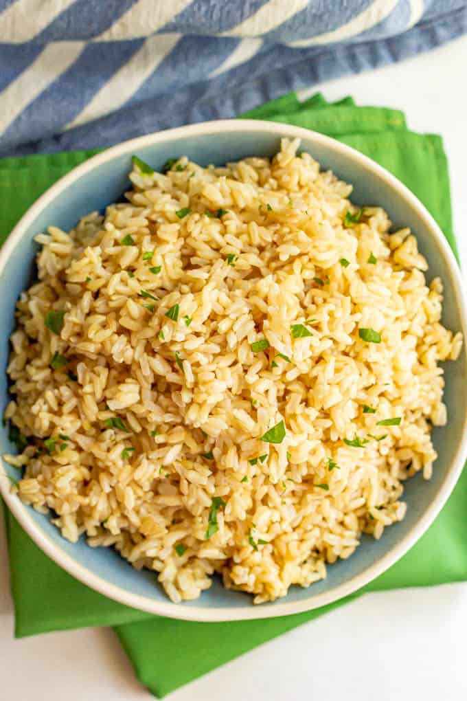 A large blue and white bowl with cooked brown rice on top of green dinner napkins