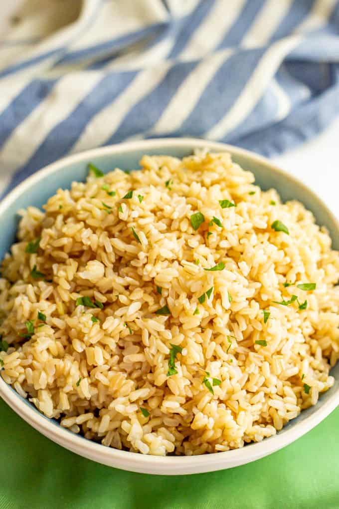 A large blue and white bowl with cooked fluffy brown rice on top of green dinner napkins