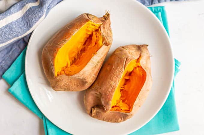 Two sweet potatoes on a white plate cut open after being cooked