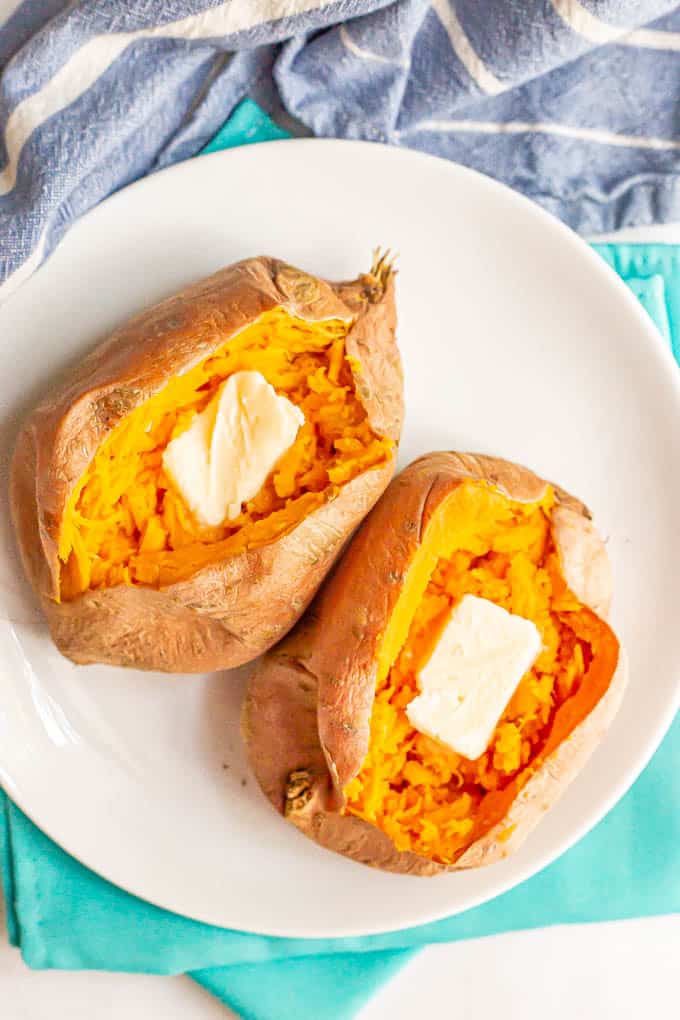 Overhead shot of two sweet potatoes on a white plate with a pat of butter in each one