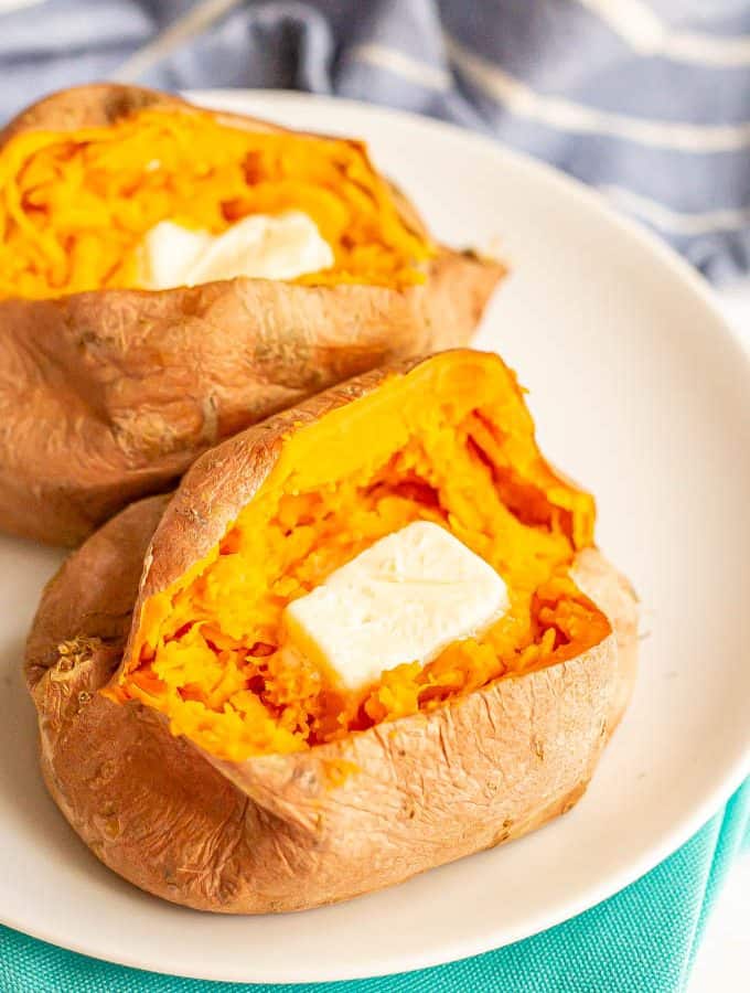 Cooked, cut open sweet potatoes on a white plate with a pat of butter in each one