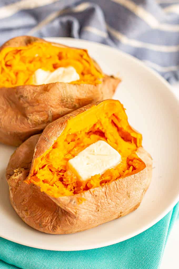Cooked, cut open sweet potatoes on a white plate with a pat of butter in each one