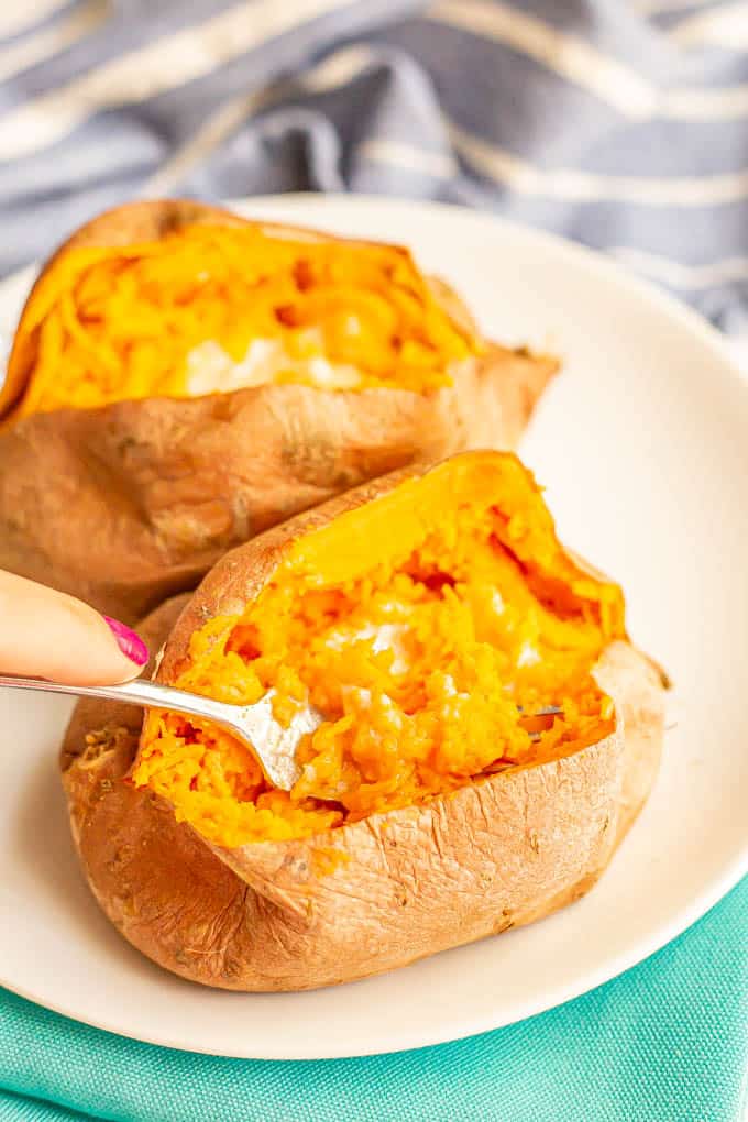 A hand picking up a forkful of sweet potato with butter from the cooked potato