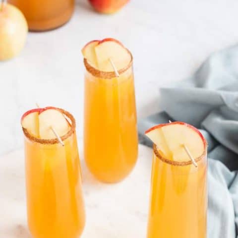 Three tall cocktail glasses with apple cider mimosa and apple garnishes