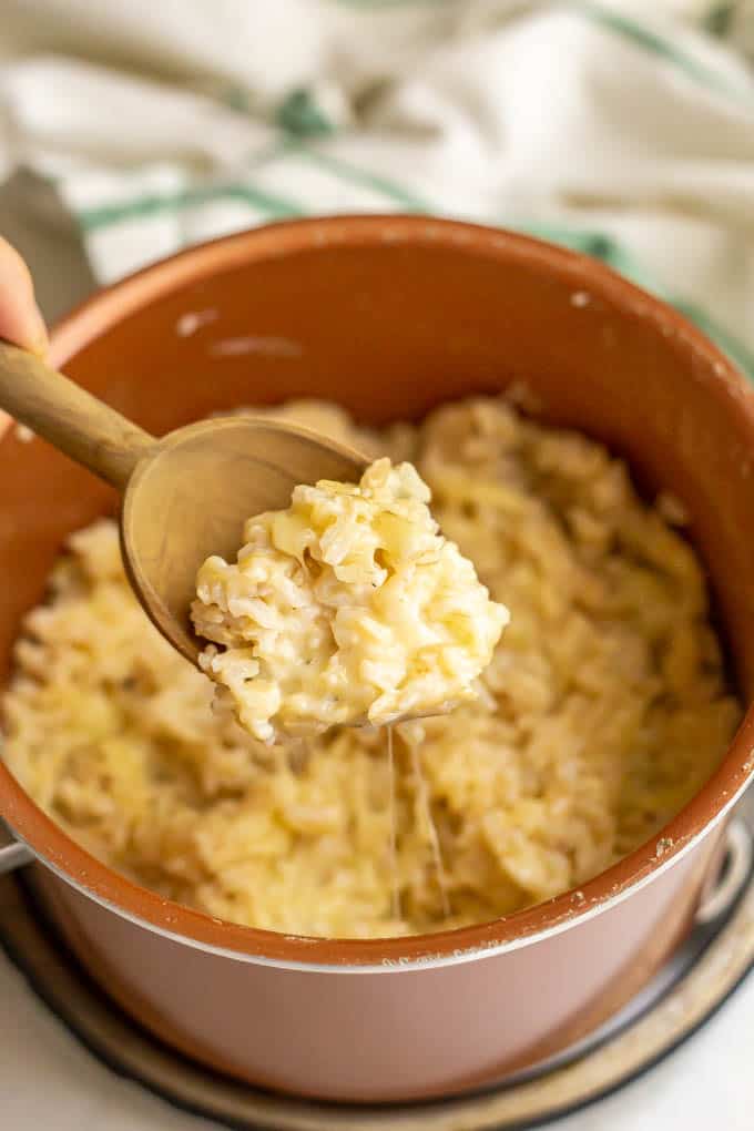 A scoop of cheesy rice being lifted out of a copper pan
