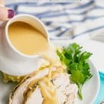 Gravy being poured over sliced turkey on a white dinner plate