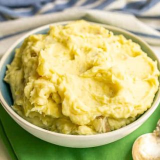 A white and blue bowl full of creamy fluffy mashed potatoes with a spoon alongside