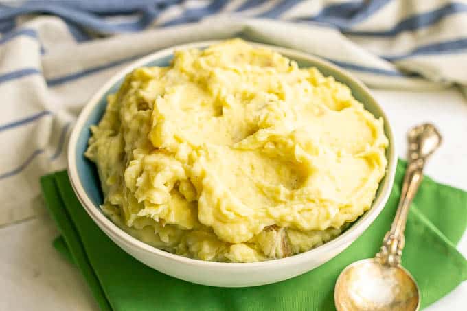 A white and blue bowl full of creamy fluffy mashed potatoes with a spoon alongside