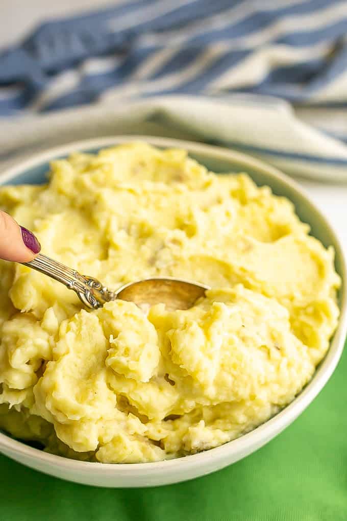 A spoon taking a scoop of creamy mashed potatoes from a white and blue serving bowl