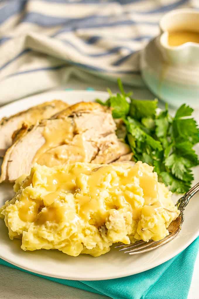 Mashed potatoes topped with gravy on a white plate with sliced turkey and a fork alongside