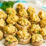 Stuffed mushrooms sprinkled with parsley and served on a white plate with a text overlay on the photo