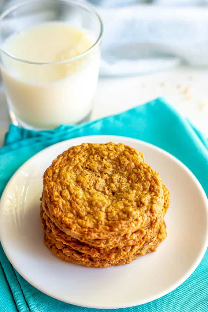 A stack of peanut butter cookies on a white plate with a glass of milk in the background