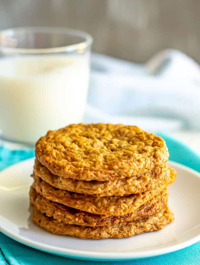 A stack of peanut butter oatmeal cookies on a white plate with a glass of milk in the background